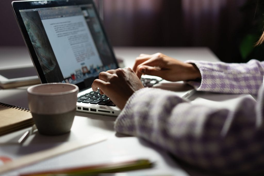 Woman Uses A Laptop While Working On A New Project Idea Late Evening. Female Hands Are Typing On Laptop Keyboard
